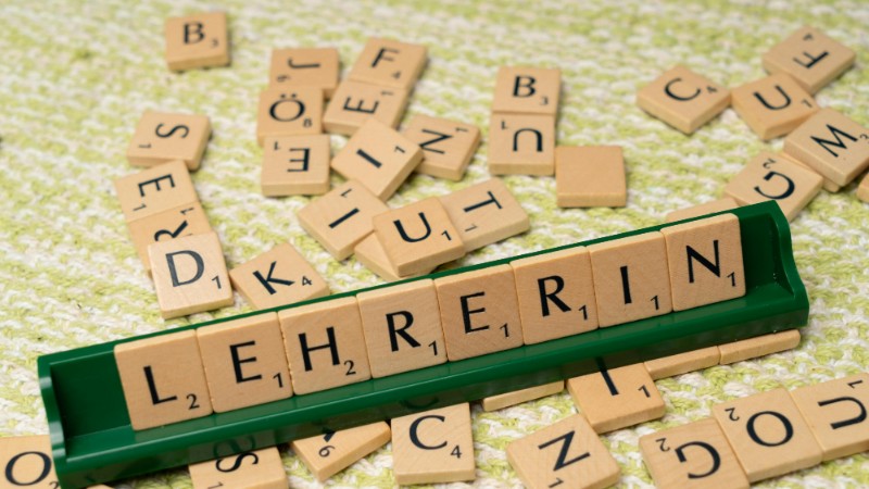 Wooden Scrabble tiles spelling 'Lehrerin' on a green holder, scattered on a textured surface., tags: deutschen - pexel